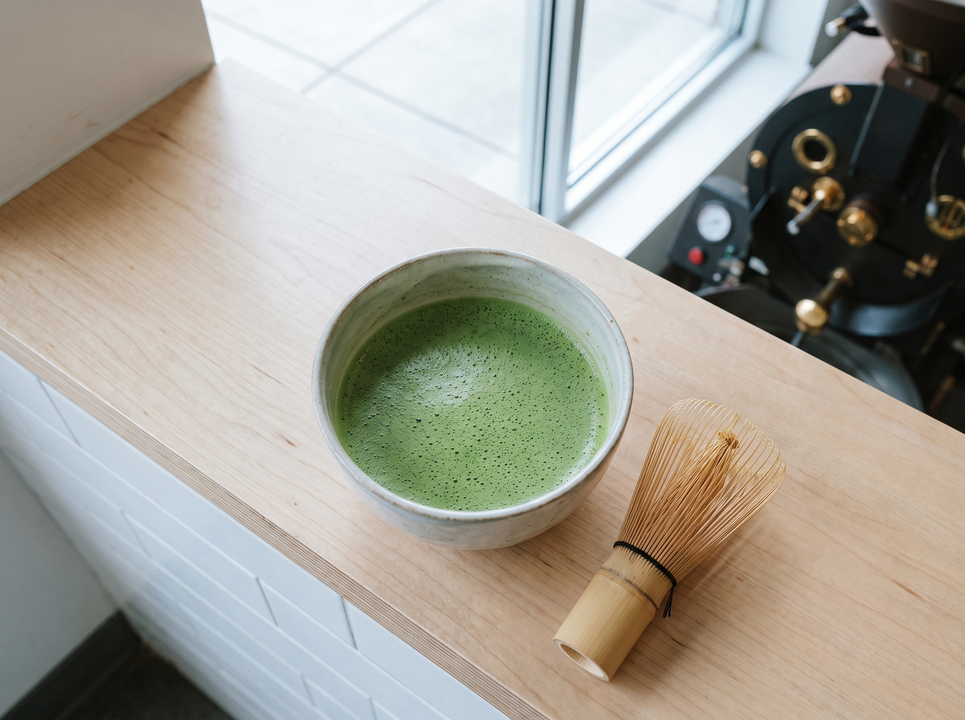 A finished bowl of matcha with even foam, chasen beside it